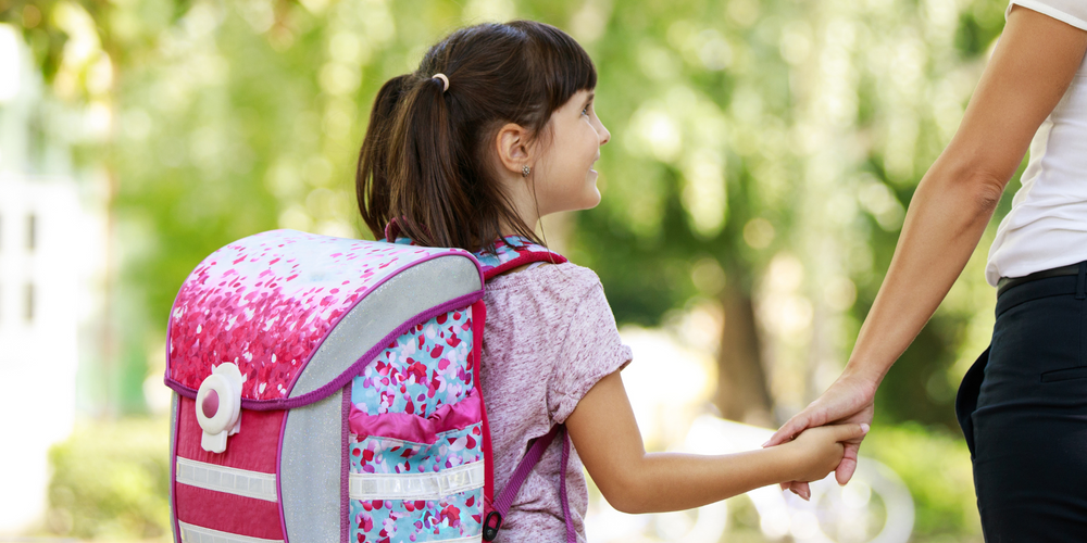 Schulranzen für Mädchen, Mädchen mit rosa Schulranzen, hält Hand einer erwachsenen Person, sommerliche Szene im Grünen, Schulweg, fröhliche Stimmung