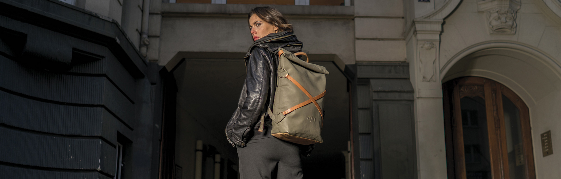 aunts&uncles, Rucksack, Frau mit Rucksack im Stadthof, lässiger Look, urbanes Umfeld, Vintage-Stil, olivgrün mit Lederdetails, nachhaltiges Design, Streetstyle, Outdoor-Atmosphäre