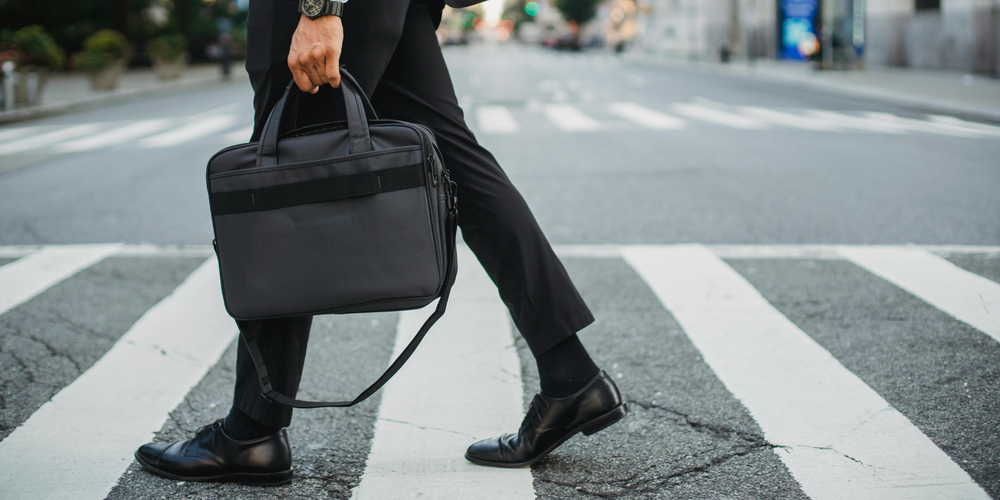 Mann in Anzug, überquert Zebrastreifen, trägt schwarze Laptoptasche, dynamische Szene