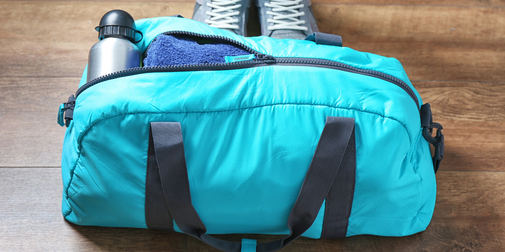 Sporttaschen, blaue Sporttasche mit schwarzem Gurt, steht auf Holzboden, Trinkflasche und Sportschuhe daneben, bereit für Sportunterricht