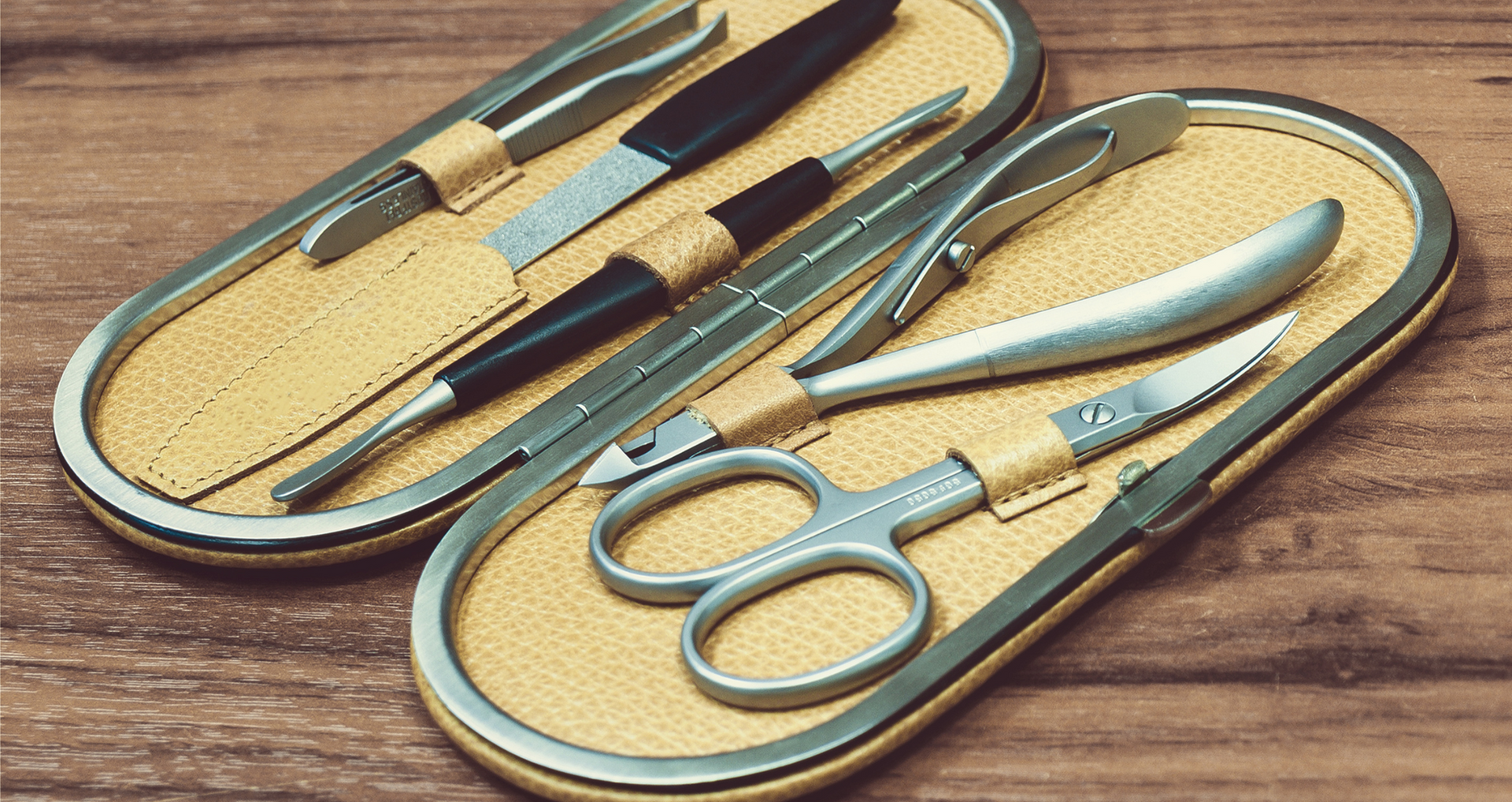 Pfeilring, Maniküre-Set, Etui geöffnet, gold-beige Innenfutter, Edelstahl-Instrumente, Schere, Feile, Pinzette, hochwertige Verarbeitung, auf Holzuntergrund