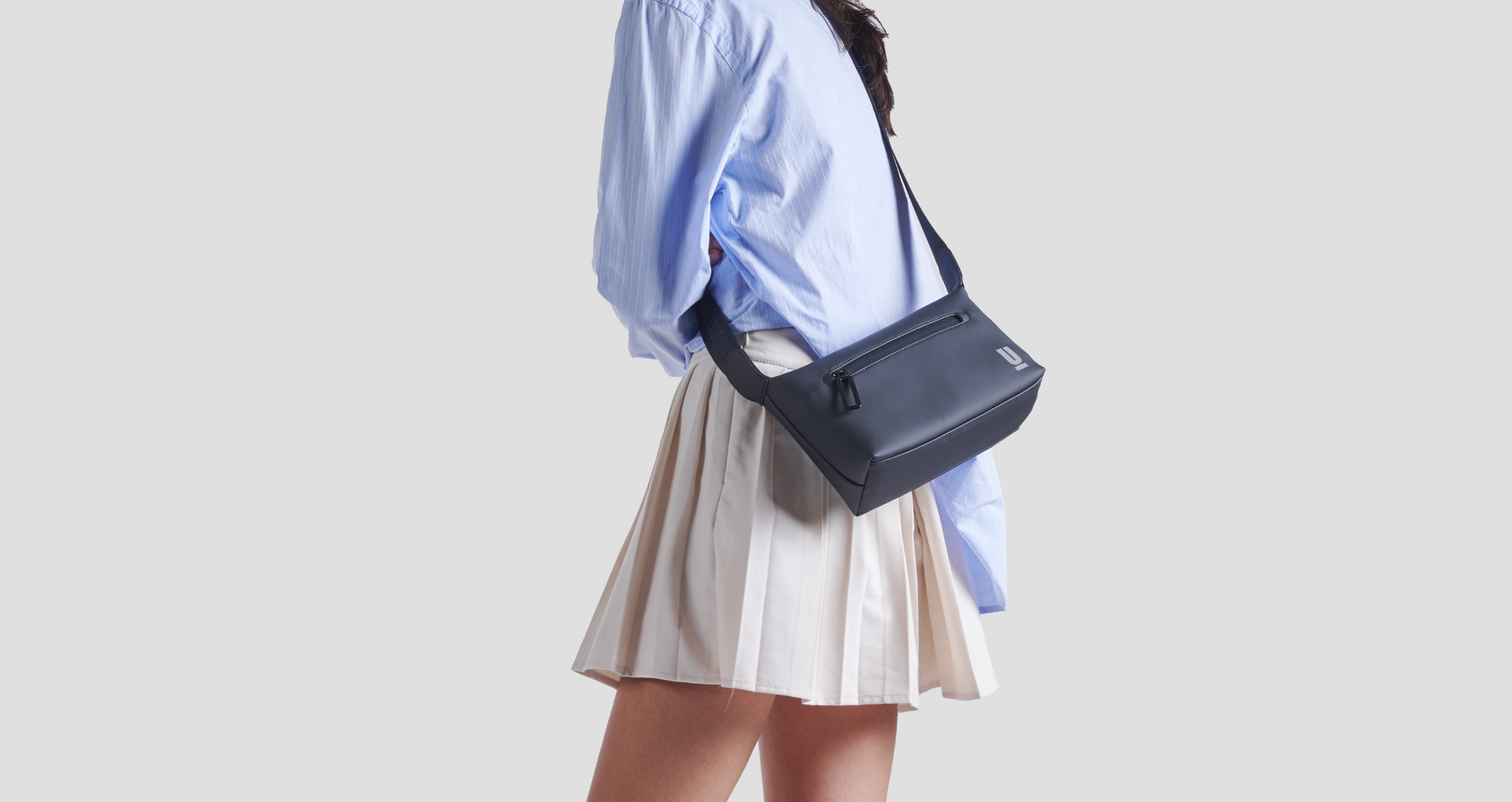 The Urban Society, Umhängetasche, schwarz, minimalistisch, Person mit blauer Hemdbluse, helle Kleidung, stilvoll, urban, clean, modern